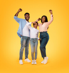 Victory concept. Excited african american family shaking clenched fists, making winner gesture, yellow background