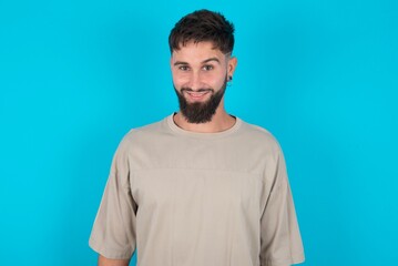 bearded caucasian man wearing casual T-shirt over blue background with nice beaming smile pleased expression. Positive emotions concept