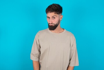 Offended dissatisfied bearded caucasian man wearing casual T-shirt over blue background with moody displeased expression at camera being disappointed by something
