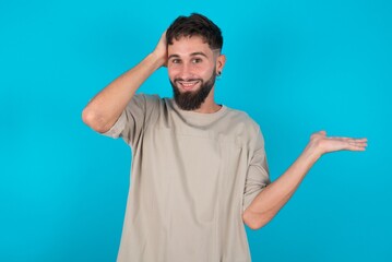 Shocked amazed surprised bearded caucasian man wearing casual T-shirt over blue background hold hand offering proposition