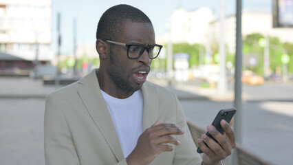 Upset African Man Reacting to Loss on Smartphone Outdoor