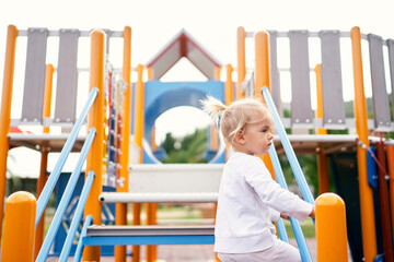 Little girl in a tracksuit climbs the stairs to the slide. High quality photo