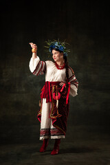 Art portrait of beautiful woman wearing traditional folk Ukrainian costume posing isolated over dark vintage background. Fashion, beauty, cultural heritage