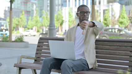 Fototapeta premium African Man with Laptop Showing Thumbs Down While Sitting Outdoor on Bench