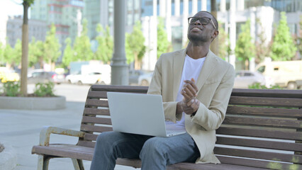 African Man with Wrist Pain Using Laptop while Sitting Outdoor on Bench