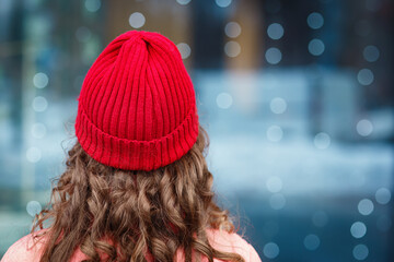 Winter mood: girl or woman  with long curly light hair in red hat and coat stands with her back to...