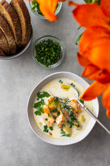 Norwegian salmon red fish soup with vegetables, herbs and cream, top view on the dining table