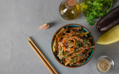 Korean style eggplant salad with sesame seeds, onions and carrots in blue bowl on gray background