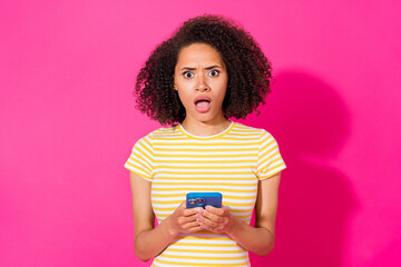 Photo portrait of nice young girl hold telephone read awful news wear trendy yellow striped look isolated on vivid pink color background