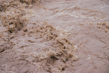 Muddy river water. Spring flood. Dirty muddy water with a whirlpool and white foam close-up.A mountain river or stream raging during a flash flood.