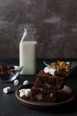 Chocolate homemade brownies with dried cranberries, walnuts, milk and marshmallows on the black background. Copy space for text