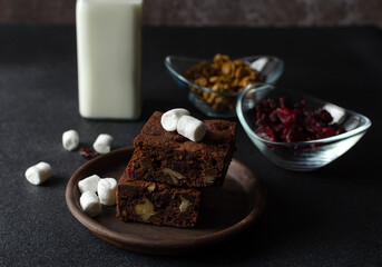 Chocolate homemade brownies with dried cranberries, walnuts, milk and marshmallows on the black background