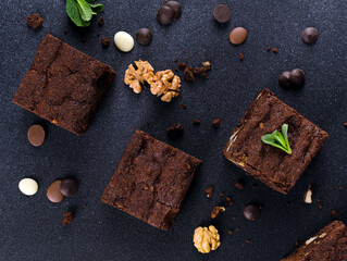 Chocolate homemade brownies with mint, walnuts and chocolate drops on the black background