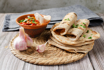 Homemade Chapati Roti Flatbread with vegetarian rajma curry, greens and garlic on wood background. Freshly baked indian street food.