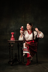 Angry woman wearing national folk Ukrainian attire posing isolated over dark vintage background. Fashion, beauty, cultural heritage, eras comparison