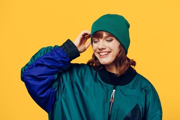 a sweet, happy woman in a stylish 90s jacket stands on a bright background and adjusts her hat on...