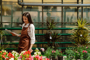 White woman holding clipboard while working with plants in greenhouse
