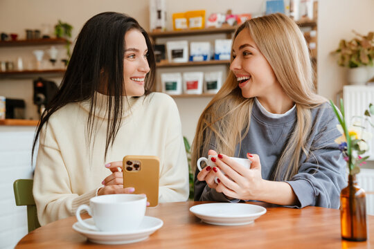 White women laughing and using cellphone while drinking tea in cafe