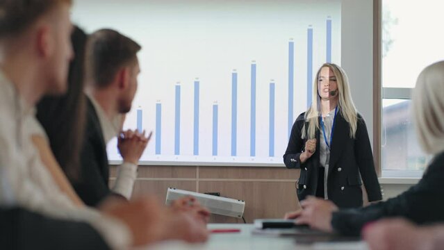 female financial analyst is speaking in front of businesspeople in business meeting