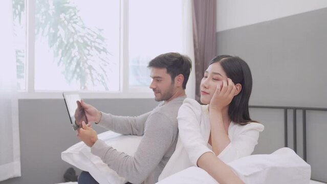 Man and woman using tablet to take pictures in bed. Young man and Young woman Couple booking hotel booking via tablet.
