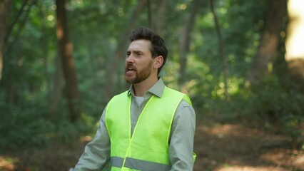 Middle aged man volunteer wearing bright green vest searching missed person in wild forest, shouting in wood