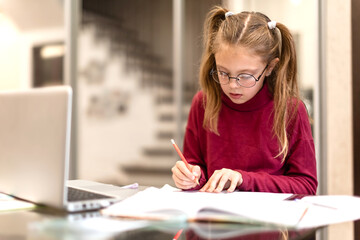 Cute student little girl seriously doing homework using laptop at home. Kids distance learning. Online education concept