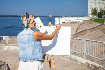 White canvas on a wooden tripod. A woman artist paints a city landscape.