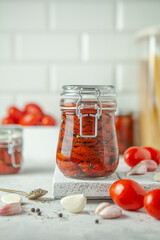 Dried tomatoes in olive oil in glass jar with ingredients around on the kitchen table