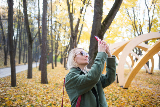 woman takes pictures on her phone in autumn park outdoor