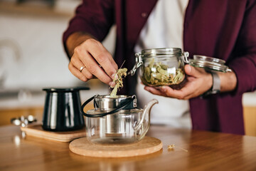 Man putting a dried herb into the teapot, preparing a tea.