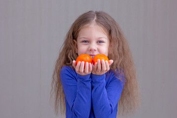 Happy and smiling child kid showing mandarins in hands on brown background looking at camera...