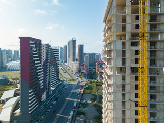 Fototapeta premium Drone view of an almost completed residential multi-storey building with a tower crane overlooking the city street on a sunny day. Multi-storey residential building is being built using a crane.