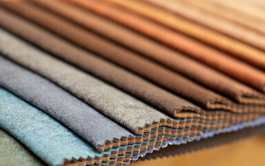 Fabric swatches in different colors are stacked for selection. A variety of shades of upholstery material for furniture and interior. Fabric texture close up. A set of multi-colored rolls of material.