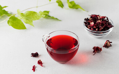 Herbal tea made from hibiscus petals in a transparent cup and a bowl of dry hibiscus.