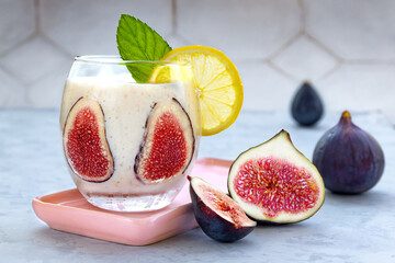 Fresh yogurt with fig slices, lemon and mint. Healthy delicious meal in glass cup on pink...