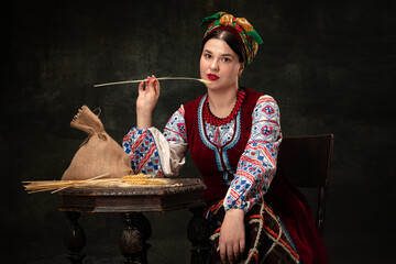 Creative portrait of beautiful Ukrainian woman wearing traditional folk costume isolated over dark vintage background. Traditions, history, fashion, beauty,