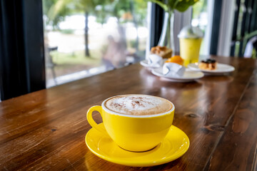 Cup of coffee and glass of water. Aroma of hot coffee latte art in yellow cup on wooden table, Blur garden background.