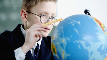 schoolboy in glasses pointing with pencil at globe in classroom.