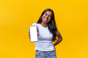 Isolated happy Indian woman looking at camera while showing phone in a yellow background.