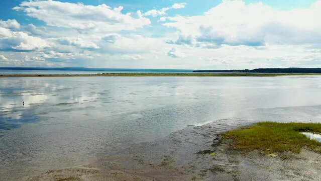 Aerial drone video, rotating from right to left, at low altitude, above the water, near herons on the shore at the Parc de la Grande Envolee in Carleton sur mer in the Baie des Chaleurs in Gaspesie