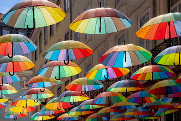 Colorful rainbow umbrella between building above pink street, Small road in city center of Lisbon,...
