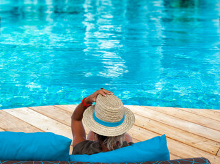 Femme au chapeau de paille sur plage en bois de piscine bleue 
