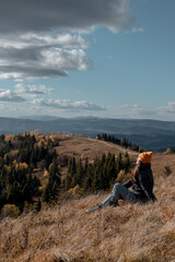 Young tourist woman is sitting on ground and enjoying mountains landscape