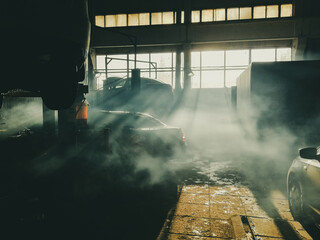 Abstract soft image of a dark room of a car workshop. A thick veil of smoke hangs in the air. The...