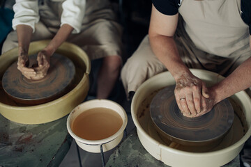 Two potters sculpt handmade earthenware on pottery wheel.