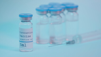 bottles with coronavirus vaccine lettering near blurred syringe on blue.