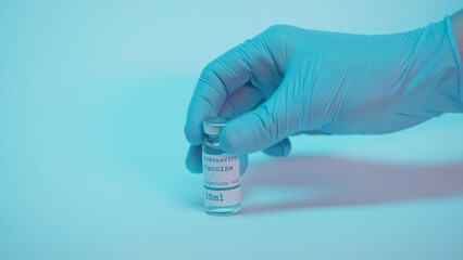 partial view of scientist in latex glove taking bottle with coronavirus vaccine lettering on blue background.