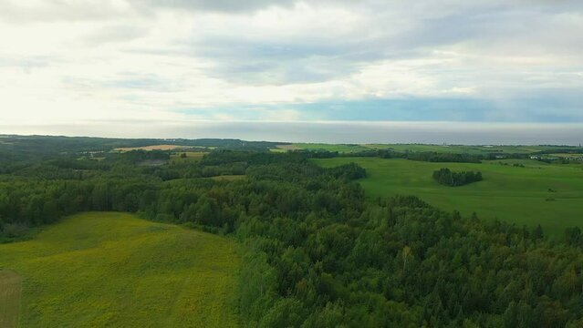 drone crane shot, rising gently above the trees and fields revealing the magnificent landscape of Petite Matane with the St-Lawrence River in the background