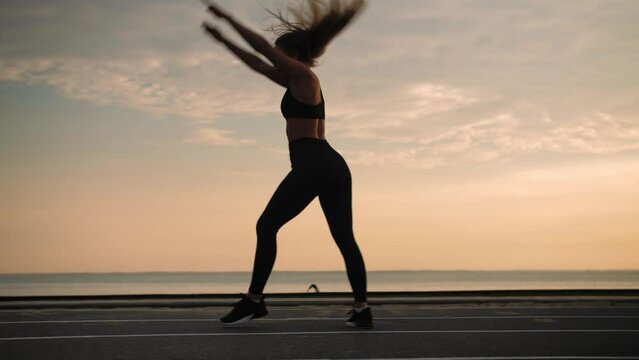 Young woman doing backflips.Girl doing acrobatic activity against the sea at sunrise. Fitness Lifestyle slow motion.Wide Shot