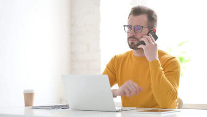 Man Talking on Phone while using Laptop in Office